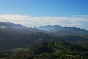 Paisaje montañoso de Cantabria con colinas verdes, bosques y montañas al fondo al atardecer