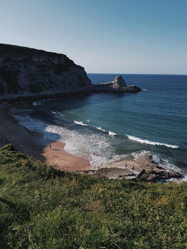 Vista de una playa en Cantabria con acantilados y mar azul, ideal para construir una segunda residencia junto al mar